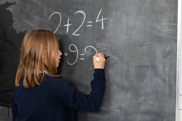 He writes on the chalkboard with chalk. Math problem. A girl at the chalkboard. - Foto, Bild