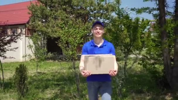 Νεαρός ελκυστικός άντρας μεταφορέας κουβαλάει ένα χαρτόκουτο - Πλάνα, βίντεο