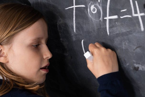 He writes on the chalkboard with chalk. Math problem. A girl at the chalkboard. - Foto, imagen