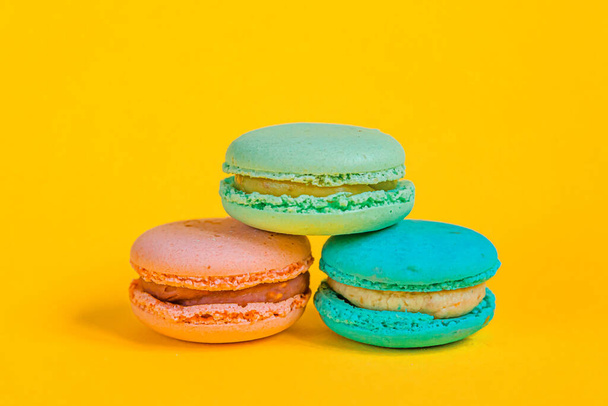 Sweet almond colorful unicorn pink blue yellow green macaron or macaroon dessert cake isolated on trendy yellow modern fashion background. French sweet cookie. Minimal food bakery concept. Copy space - Photo, Image