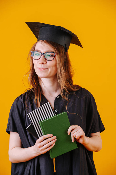 Portrait of girl in academic dress with a diploma in her hands on a yellow background - Foto, immagini