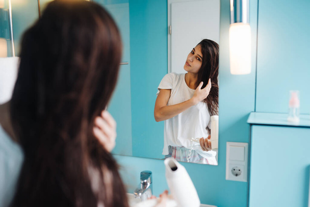 Πορτρέτο της νεαρής γυναίκας που χρησιμοποιεί στεγνωτήρα μαλλιών στο μπάνιο - Φωτογραφία, εικόνα