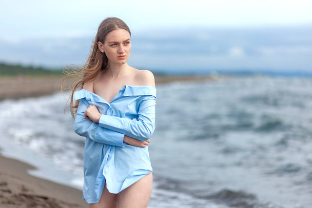 Όμορφη νεαρή ξανθιά κοπέλα σε ένα μπλε πουκάμισο χαλαρώνοντας στη θάλασσα, θέρετρο - Φωτογραφία, εικόνα