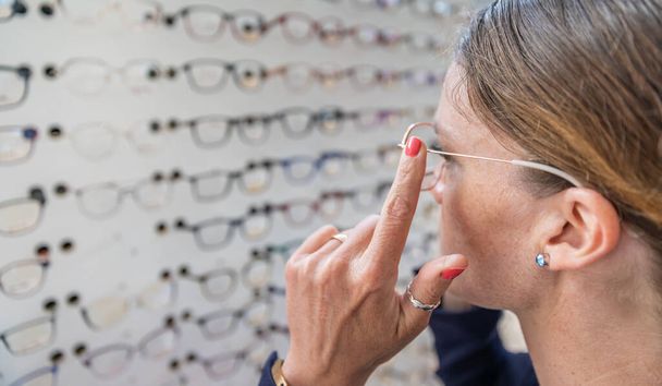 woman chooses and tries glasses in optics store. copy space - Photo, Image