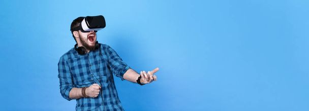 homem barbudo em óculos de realidade virtual, jogando emocionalmente atiradores em VR em fundo azul
 - Foto, Imagem