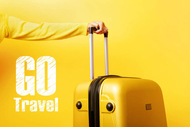 woman holding yellow suitcase in hand over yellow background, go travel concept - Fotó, kép