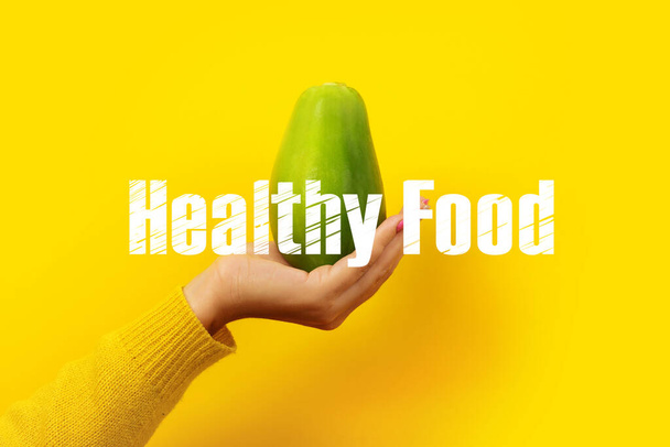 female hand holding green papaya on yellow background, healthy food concept - Photo, Image