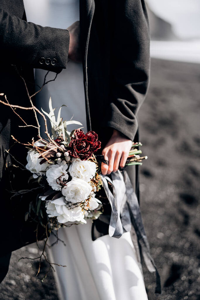 Destinazione Matrimonio Islanda. Primo piano del bouquet delle spose, lo sposo abbraccia la sposa per la vita
. - Foto, immagini