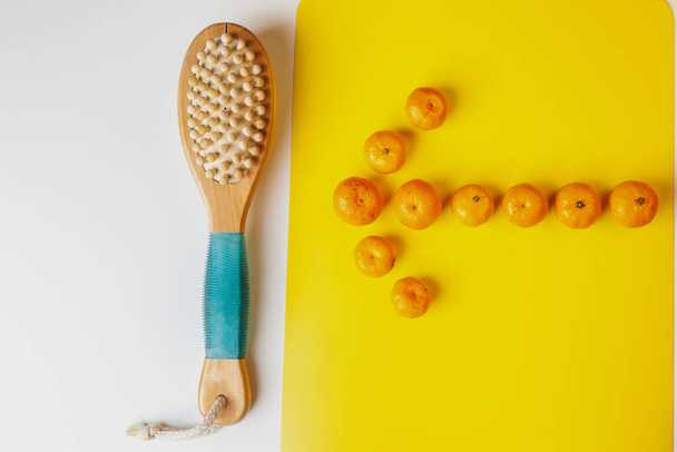 乾燥ボディマッサージのための抗セルライトブラシ。オレンジは矢印の形で配置されています。健康的なライフスタイル,セルライトの予防. - 写真・画像