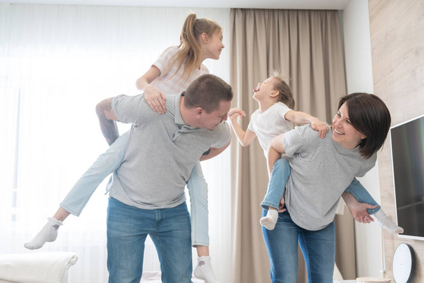 Madre e padre giving figlie cavalluccio in soggiorno
 - Foto, immagini