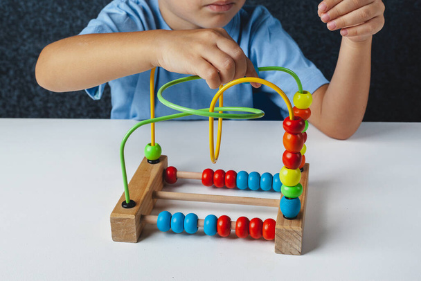 Child plays Montessori game. Kid collects wooden toy sorter. Multicolored geometric shapes, circle, square, triangle, rectangle. - Photo, Image