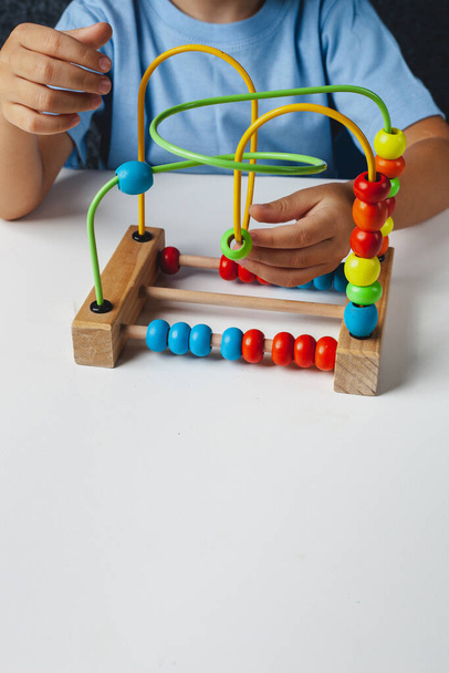 Child plays Montessori game. Kid collects wooden toy sorter. Multicolored geometric shapes, circle, square, triangle, rectangle. - Photo, Image