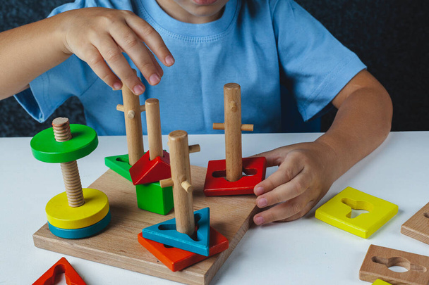 A gyerek Montessori játékot játszik. A gyerek fa játékválogatót gyűjt. Sokszínű geometriai formák, kör, négyzet, háromszög, téglalap. - Fotó, kép