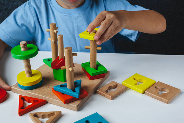 Child plays Montessori game. Kid collects wooden toy sorter. Multicolored geometric shapes, circle, square, triangle, rectangle. - Foto, imagen