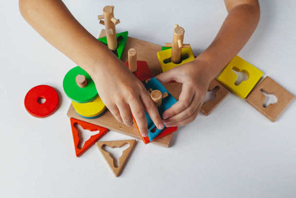 子供はモンテッソーリのおもちゃを演じる。白い背景に多色論理ソーター。赤ちゃんの手を閉じる。木製の幾何学的な形の円、正方形、三角形、長方形。上からの眺め - 写真・画像
