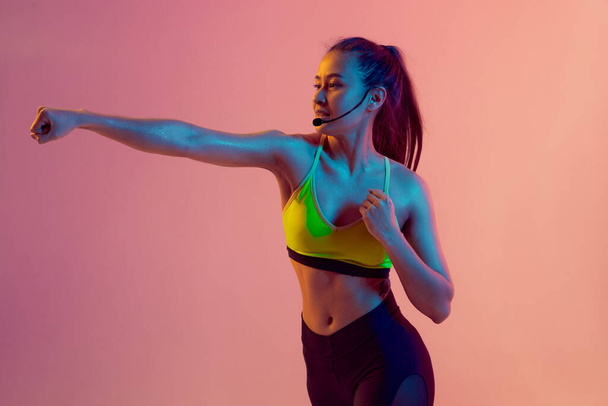 Cute girl fitness instructor teaches Boxing or body combat online training remotely on a bright neon background. - Fotografie, Obrázek