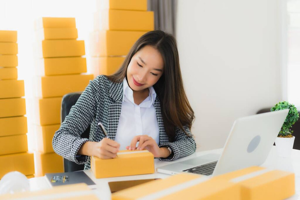 Portret piękny młody azjatycki biznes kobieta praca z domu z laptopem telefon komórkowy z pudełkiem kartonowym gotowy do wysyłki zakupy online - Zdjęcie, obraz
