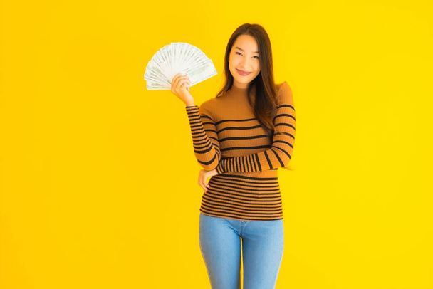 Portret piękna młoda azjatycka kobieta szczęśliwy uśmiech i bogaty z dużą ilością gotówki w ręku na żółtym odizolowanym tle - Zdjęcie, obraz