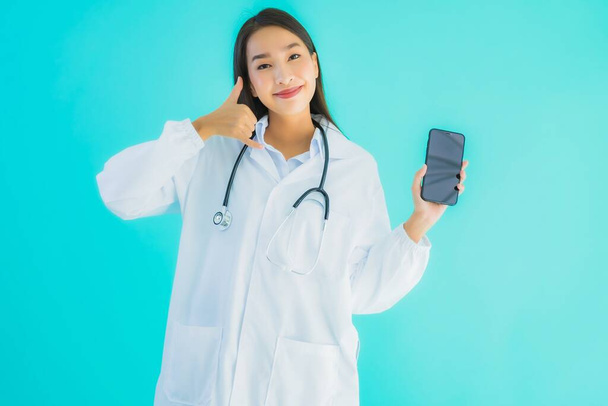 Портрет красива молода азіатська жінка-лікар використовує мобільний смартфон для клініки або лікарні на синьому ізольованому фоні
 - Фото, зображення