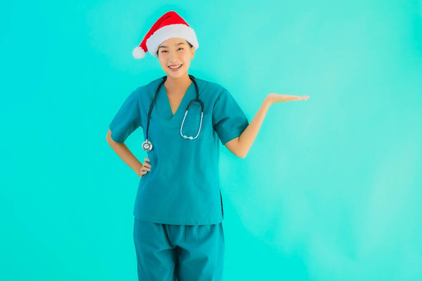 Portret mooi jong aziatisch arts vrouw dragen kerst hoed met glimlach gelukkig op blauw geïsoleerde achtergrond - Foto, afbeelding