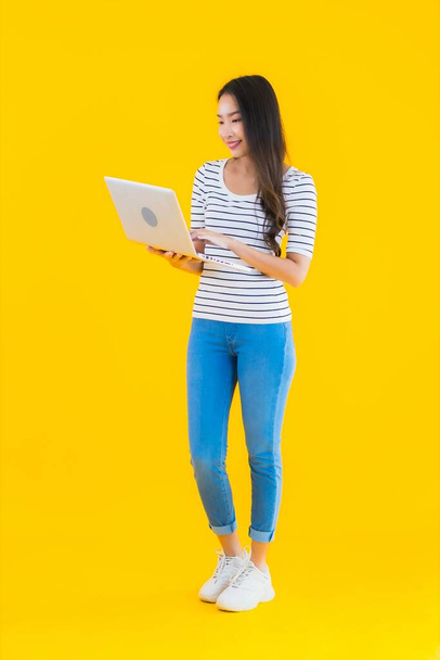 Porträt schöne junge asiatische Frau verwenden Laptop oder Notebook für Arbeit und Studium auf gelbem Hintergrund isoliert - Foto, Bild