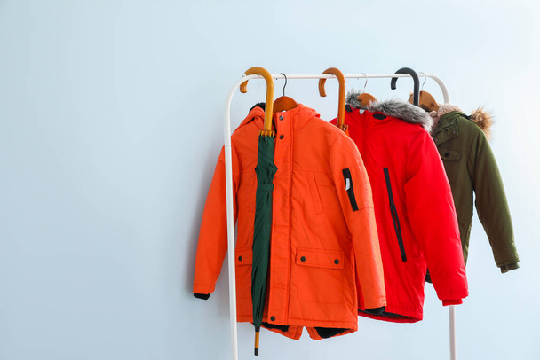 Stylish umbrellas and clothes on rack near color wall - Photo, Image