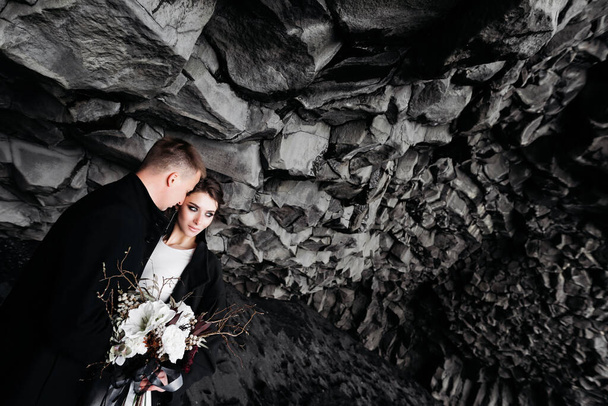Destination Island Hochzeit. Hochzeitspaar unter einem Stein aus Basaltsteinen. Braut und Bräutigam am schwarzen Strand von Vik. - Foto, Bild