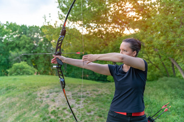 archery in nature, young woman aiming an arrow at a target - Photo, Image