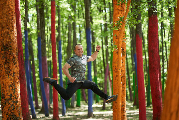 Caucasian man jumping for joy in a forest with colored trees - Foto, Imagen