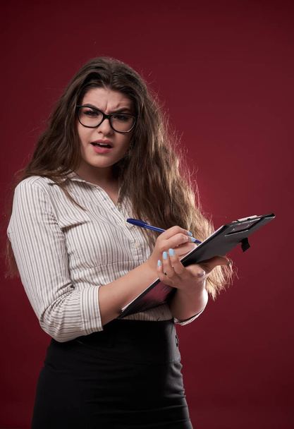 Businesswoman with glasses and a clipboard, unsure what to do next - Foto, imagen