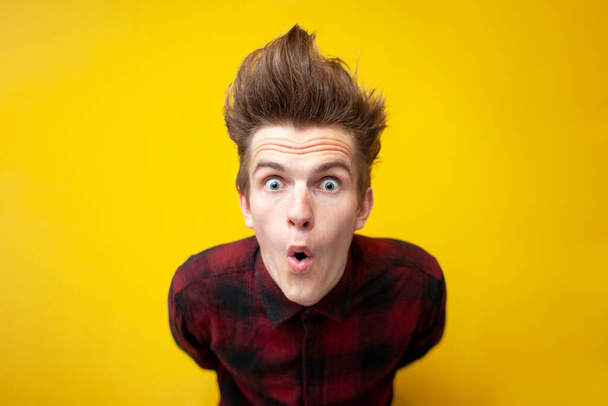 young shocked guy surprised at yellow isolated background, hipster with funny hairstyle in shock, close-up - Photo, Image