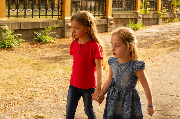Siostry, zdjęcie z zewnątrz od dwóch małych dziewczynek. Dwie małe dziewczynki chodzą po parku za rękę. Siostry na spacer latem lub jesienią na ulicy. Dziewczyny, dzieci, przyroda. Koncepcja rodziny. - Zdjęcie, obraz