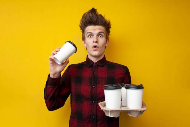 Genç şokta olan adam canlandırıcı kahve içiyor ve sarı izole bir arka plana şaşırıyor. Bir adam enerji içeceği içiyor. - Fotoğraf, Görsel