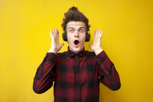překvapený šokovaný chlap poslech hudby na sluchátka na žlutém izolovaném pozadí - Fotografie, Obrázek