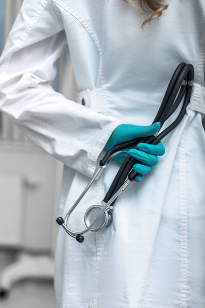 Doctors hand in white coat holding a phonendoscope on the background of a hospital ward. Medicine, life saving, general practitioners. - Photo, image
