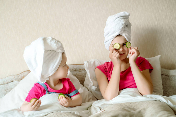 Beautiful girl with facial mask of cucumber. face mask, children laugh, funny faces, first makeup for a teenager.Morning in bed after bath. white towel - 写真・画像
