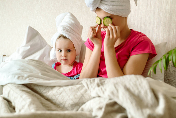 Beautiful girl with facial mask of cucumber. face mask, children laugh, funny faces, first makeup for a teenager.Morning in bed after bath. white towel - Photo, Image
