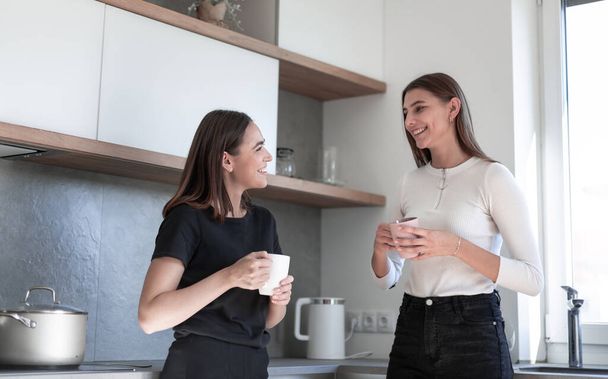 Two young laughing women standing at kitchen and enjoy - Foto, afbeelding