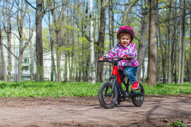 Little cute girl is riding a bicycle in the spring park. Child learning to drive a bicycle on a path outside. - Fotó, kép