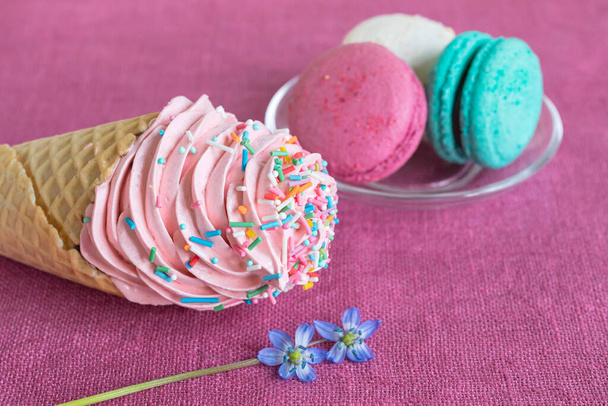White, blue and purple macaroons, waffle cone with homemade marshmallow and spring flower on a linen napkin. Macarons or macaroons is French or Italian dessert. Close-up. Selective focus - Zdjęcie, obraz