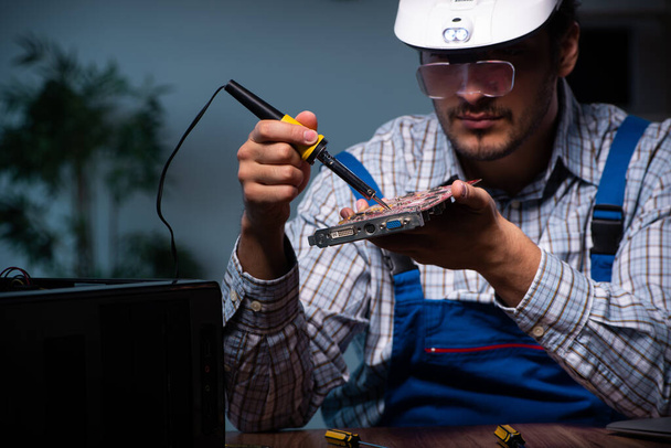 Νεαρός τεχνίτης επισκευάζει υπολογιστές στο εργαστήριο τη νύχτα - Φωτογραφία, εικόνα