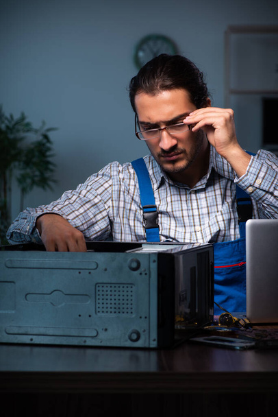 Joven técnico masculino reparando el ordenador en el taller por la noche
 - Foto, Imagen