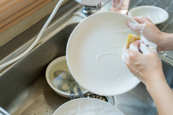 Жінка використовує посудомийну рідину на жовтій губці крупним планом. Господар миє брудний посуд в раковині крупним планом. Концепція домашнього господарства та повсякденного домашнього завдання, фото з копією
. - Фото, зображення