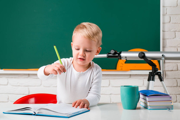 School kids against green chalkboard. Little student boy happy with an excellent mark. Happy cute industrious child is sitting at a desk indoors. - Фото, изображение