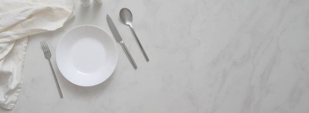 Bovenaanzicht van moderne eettafel met bord, bestek, servet, kruidenflesjes en kopieerruimte op marmeren bureau   - Foto, afbeelding