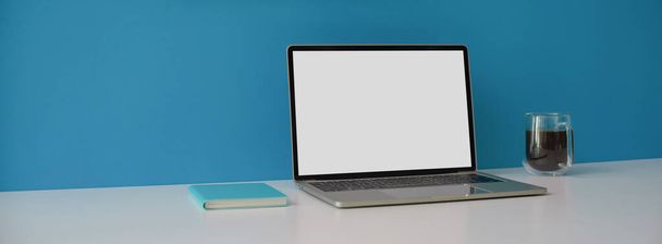 Ausschnitt aus dem kreativen Arbeitsbereich mit Laptop-Attrappe, Notizbuch und Kaffeebecher auf weißem Schreibtisch mit blauem Wandhintergrund - Foto, Bild