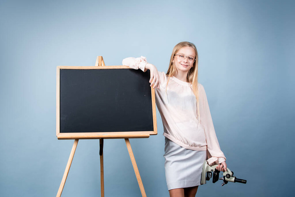 First of September. Day of knowledges. Cute blonde girl standing near blackboard wearing a school uniform. Pretty little schooler girl going to her first lesson. - Foto, Imagem