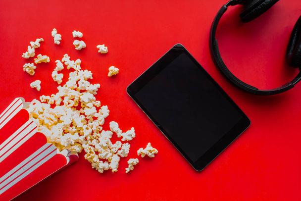 Una tableta sobre un fondo rojo con palomitas de maíz y auriculares
 - Foto, imagen