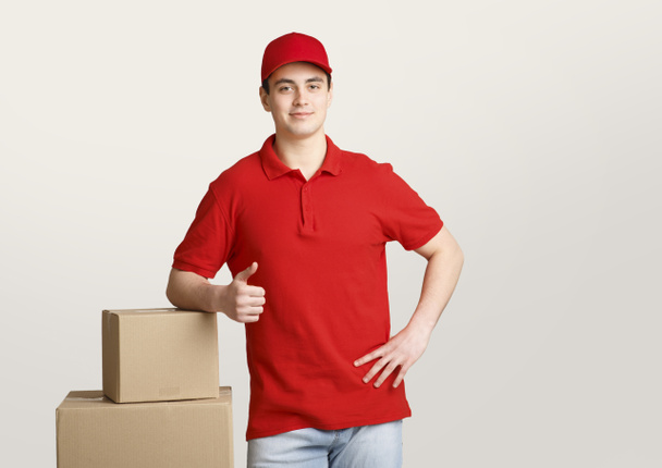 Fast delivery. Courier leans on boxes and shows sign perfectly with his hand - Photo, Image