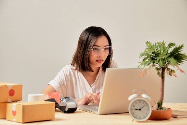 Молода приваблива азіатська жінка онлайн-продавець працює на замовлення перевірки ноутбуків в Інтернеті вдома, готуючись до доставки з дому
 - Фото, зображення